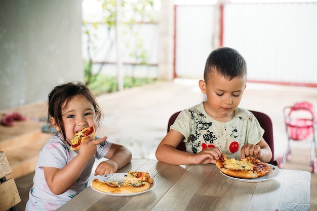 女の子と男の子、ストリートチルドレンはとても食欲をそそるミニピザを食べます