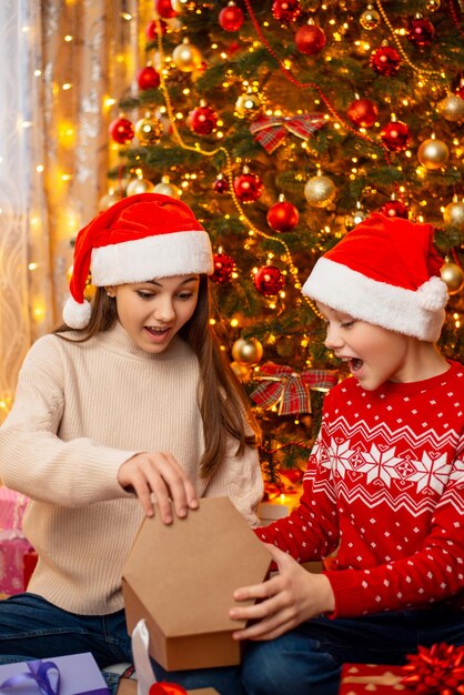 Girl and boy under Christmas tree opening presents happy and surprised to get nice presents