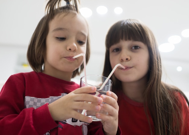 Girl and boy drinking water from glass using straw