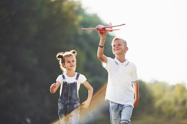 Girl and boy having fun outdoors with red toy airplane in hands.