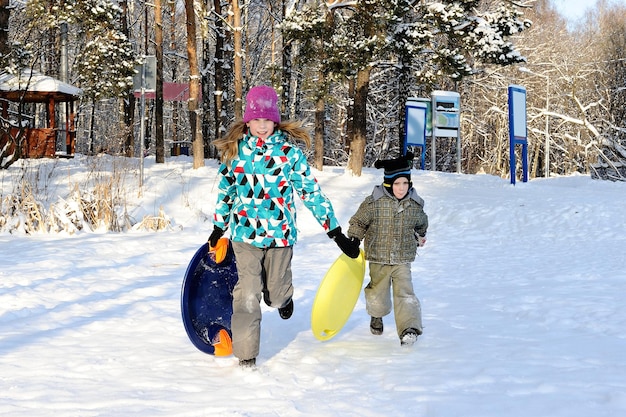 Girl and boy riding with hills on sleds on winter weather