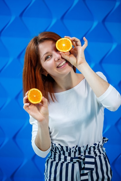 Girl on a bright blue background in a white blouse with oranges in hand