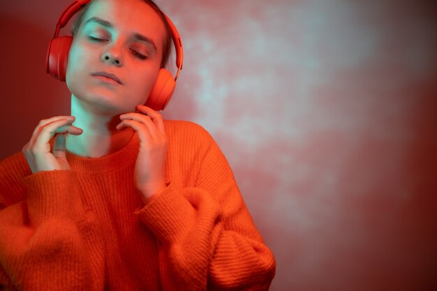 A girl in bright colored lighting listens to music with headphones