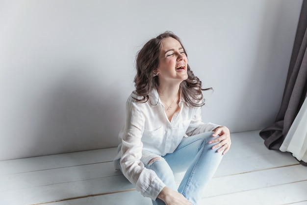 Girl in bright room sitting against white wall