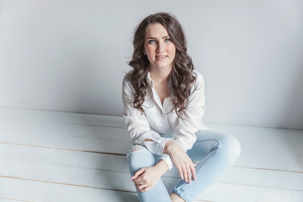 Girl in bright room sitting against white wall