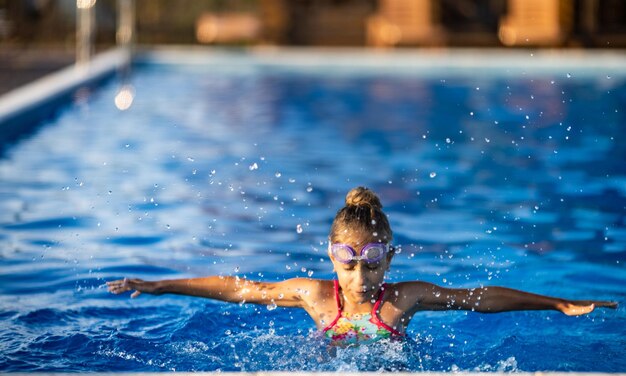 A girl in a bright swimsuit with swimming goggles dives into a pool with clear transparent water