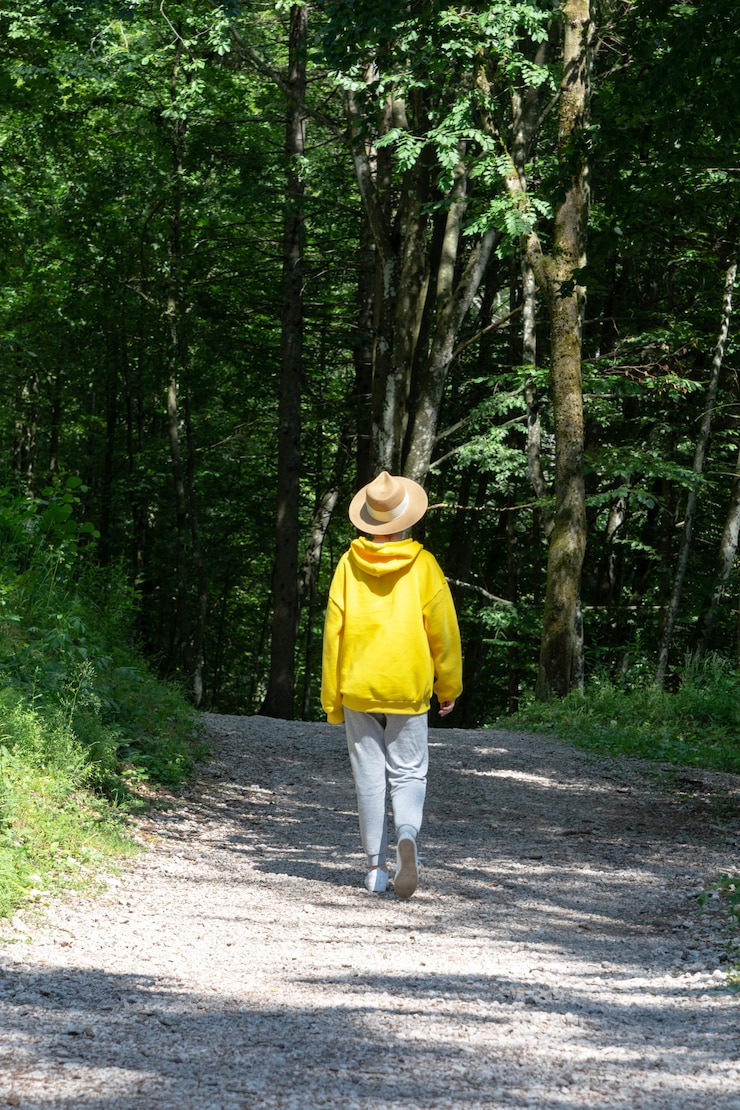 Photo a girl in a bright yellow hoodie with a hat is walking along a path in the forest.