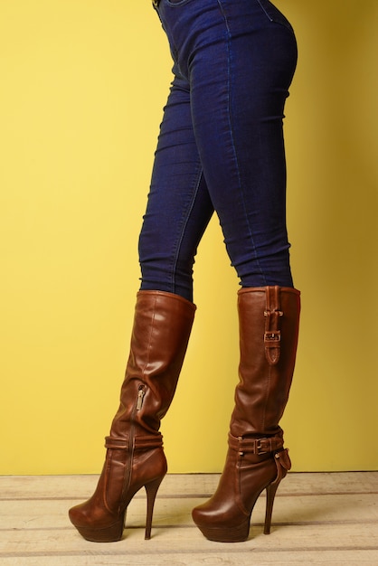 Girl in brown boots and jeans stands on a white wooden floor near a yellow wall