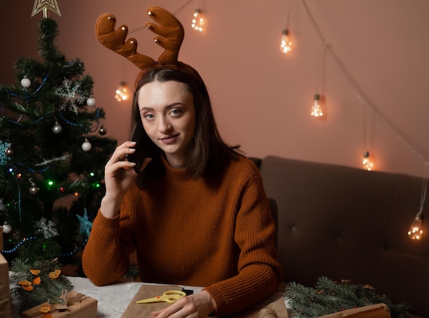 a girl in a brown sweater holds a phone and packs gifts for the new year