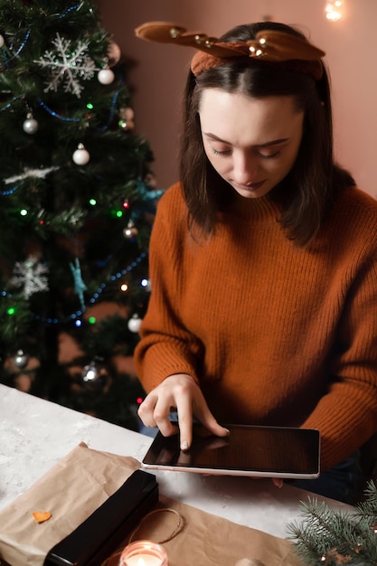 a girl in a brown sweater holds a tablet and packs gifts for the new year