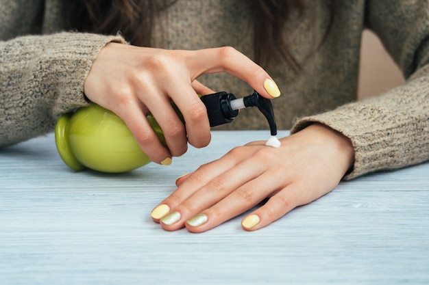 Girl in brown sweater with yellow manicure applying hand cream, close-up