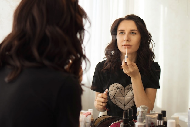 Girl brunette puts makeup in front of the mirror, reflection in the mirror