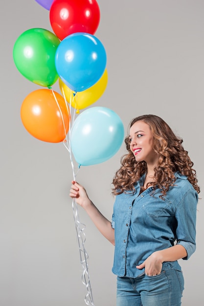 The girl and bunch of colorful balloons on gray wall