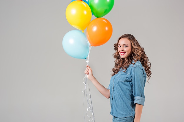 The girl and bunch of colorful balloons on gray  wall