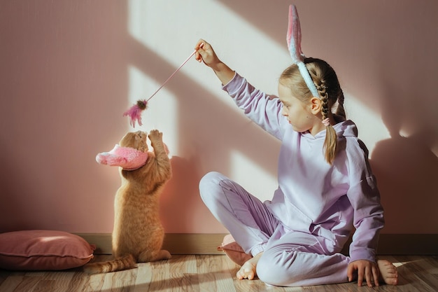 A girl in bunny ears plays with a cat toy