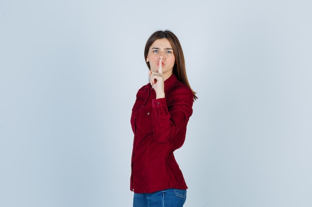 girl in burgundy shirt showing silence gesture and looking serious