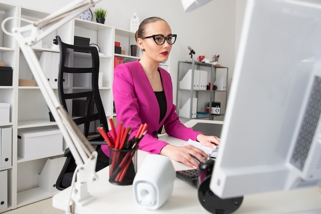 A girl in a business style works at a computer in office