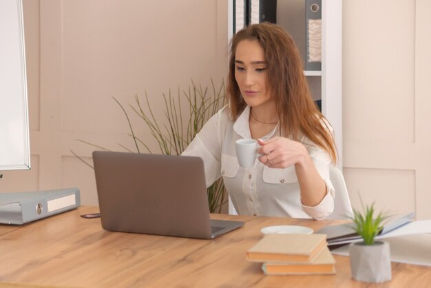 A girl in a business style works at a computer in the office