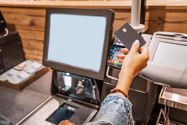 The girl buyer applies a credit card to the pos terminal to pay for purchases at the selfservice checkout