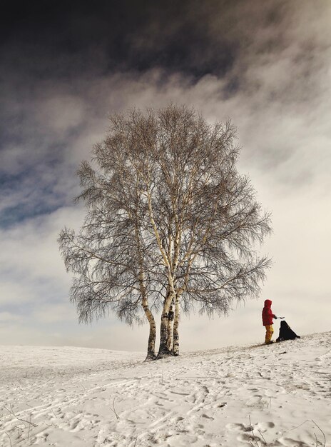 girl by bare tree on snow covered land against sky