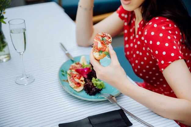 カフェ屋外のファッショナブルな女の子でサーモンサンドイッチを保持している若い女性のカフェトリミングビューの女の子