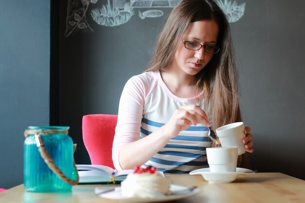 ノートブックで一杯のコーヒーのためのカフェの女の子