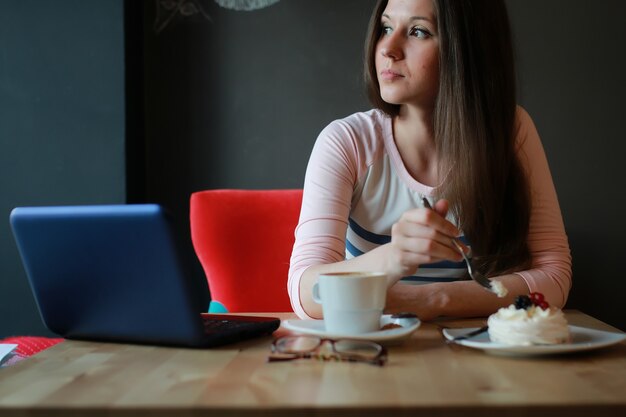 ノートブックで一杯のコーヒーのためのカフェの女の子