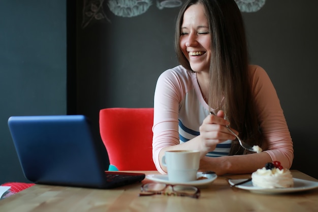 ノートブックで一杯のコーヒーのためのカフェの女の子