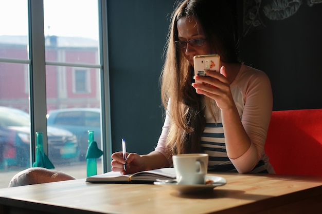 ノートブックで一杯のコーヒーのためのカフェの女の子