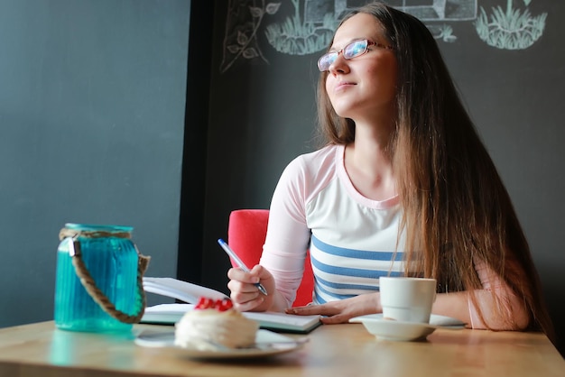 ノートブックで一杯のコーヒーのためのカフェの女の子