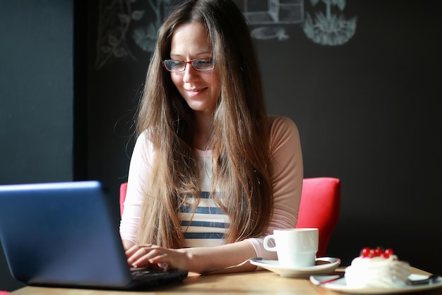 ノートブックで一杯のコーヒーのためのカフェの女の子