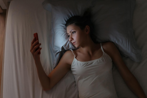 사진 여자는 밤에 침대에서 잠을 못 자고 휴대전화를 확인한다