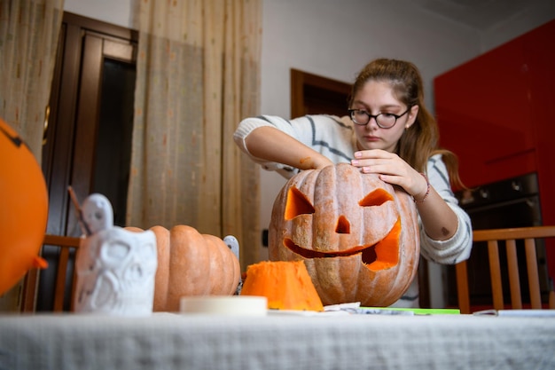 キッチンでハロウィーンの休日の装飾のためにジャックランタンに大きなオレンジ色のカボチャを彫る女の子パーティーのための装飾