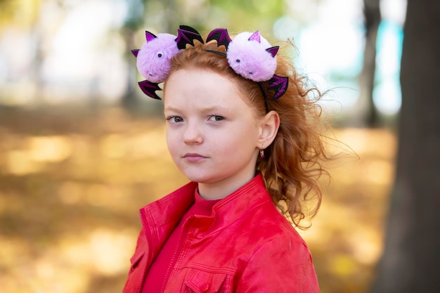 A girl in casual clothes and with a headband with Halloween horns looks at you menacingly