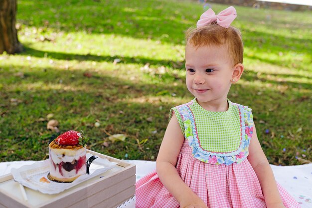 ピクニック中に庭でおいしいイチゴのケーキで 2 歳の誕生日を祝う女の子