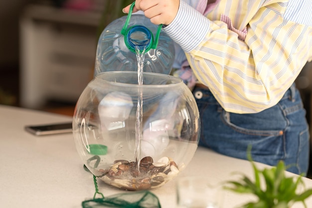 The girl changes the water in the aquarium. a girl pours clean water from a bottle into an aquarium.