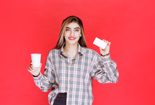 Ragazza in camicia a quadri che tiene una tazza di caffè e presenta il suo biglietto da visita