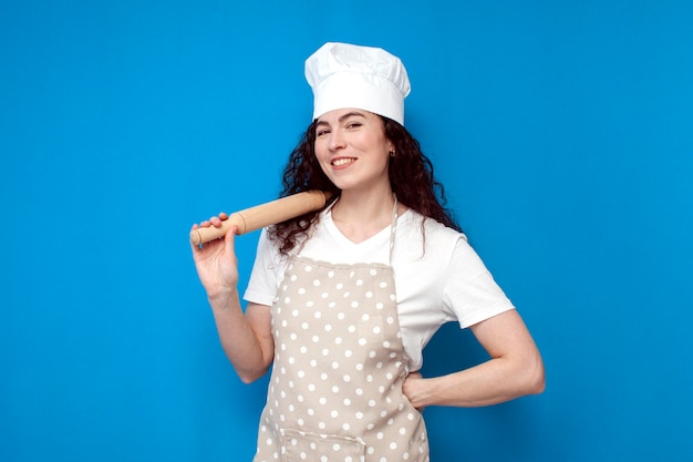 Girl chef in uniform holds items for cooking and smiles on blue background