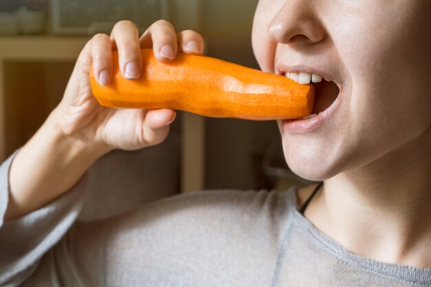 Girl chews orange carrot. Healthy food