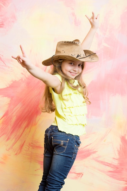 Girl child in cowboy hat and jeans showing horns gesture