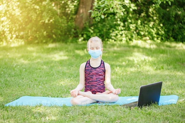 Girl child in face mask doing sport workout outdoor online video yoga on internet social distance