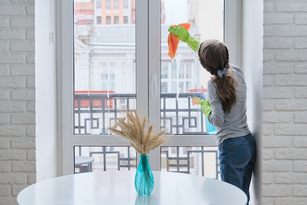 Girl child in gloves with spray detergent with rag cleaning house