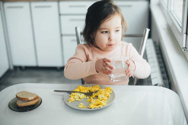 Una bambina è in cucina a bere acqua c'è un piatto con una frittata accanto