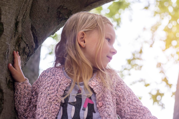 Girl child is played sitting high on a tree in the park