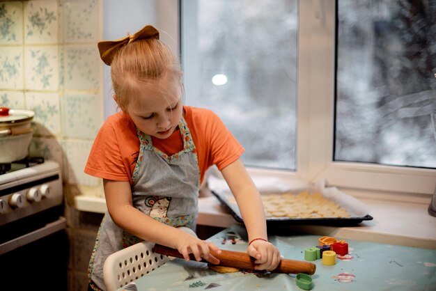 Foto una bambina fa i biscotti dall'impasto in cucina