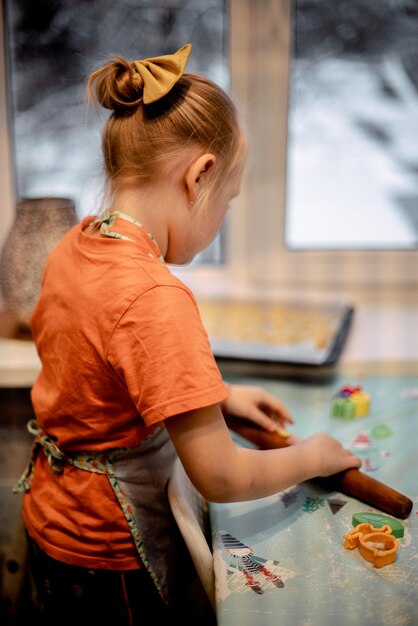 Foto una bambina fa i biscotti dall'impasto in cucina