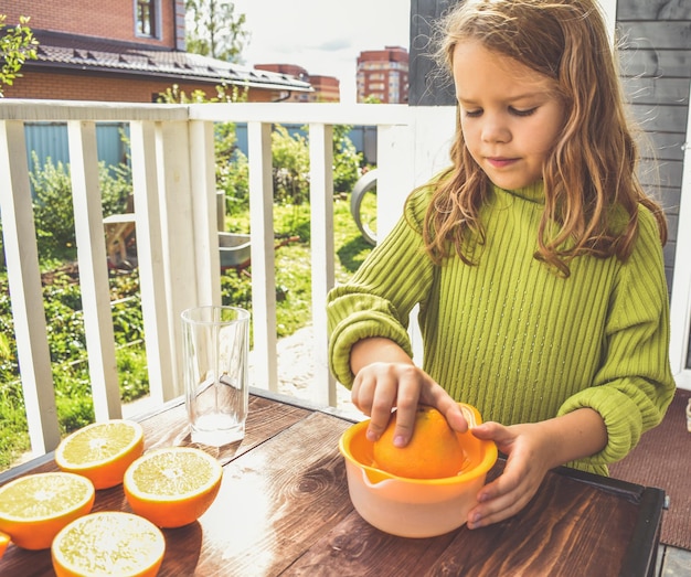The girl child makes freshly squeezed orange juice on a manual juicer