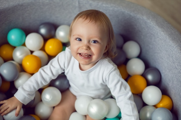 La bambina si siede in una piscina con palline di plastica colorate