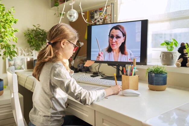 Girl child sitting at home at table with computer listening online lesson