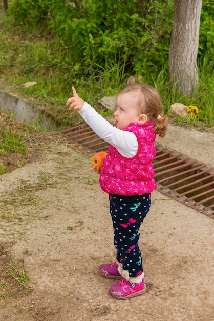 Girl child stands on the street and shows her hand and finger up to the sky